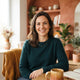 A friendly woman smiling in a bright, modern room with warm terracotta and amber decor, representing a satisfied customer.